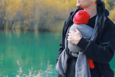 Çekici, genç bir baba ve bebeği açık havada asılıymış. İnsan çocuğunu taşıyor ve sonbahar dağ gölünde seyahat ediyor. Bebek giyme konsepti