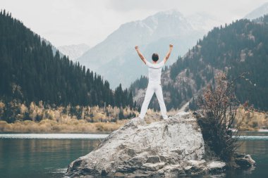 Bir adam büyük bir taşın üzerinde duruyor ve ellerini havaya kaldırıyor. Dağların karlı zirveleri. , Issyk şehri, Kazakistan