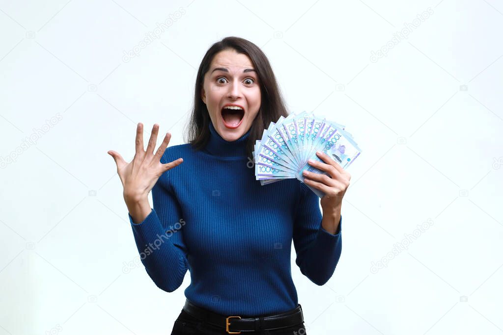 A happy woman rejoices in tenge money against a homogeneous background.