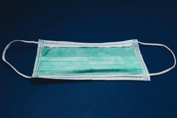 Medical surgical mask on blue paper background, Prevent Covid-19, protection factor for virus. Dark toned low key photo