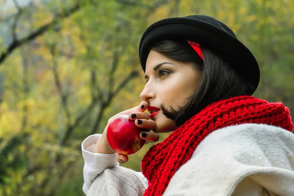 Siyah şapkalı güzel bir kadın ve elinde kırmızı bir elma olan kırmızı bir eşarp. Sonbahar açık hava pikniği — Stok fotoğraf