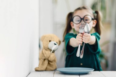 Küçük şirin çocuk çatal ve kaşıkla el ele tutuşup çatal bıçak kullanmayı öğreniyor..