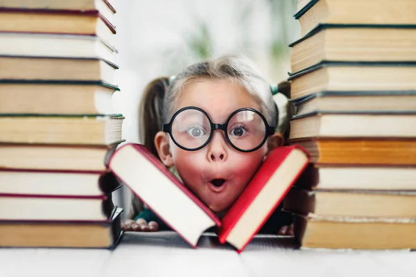 Kitap yığınının arasında komik gözlüklü, meraklı yüzlü okul öncesi kızı..