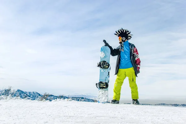 戴着滑雪面罩 戴着护目镜 头戴毛皮大莫霍克帽 背景是天空和冬季雪山的快乐雪人 — 图库照片