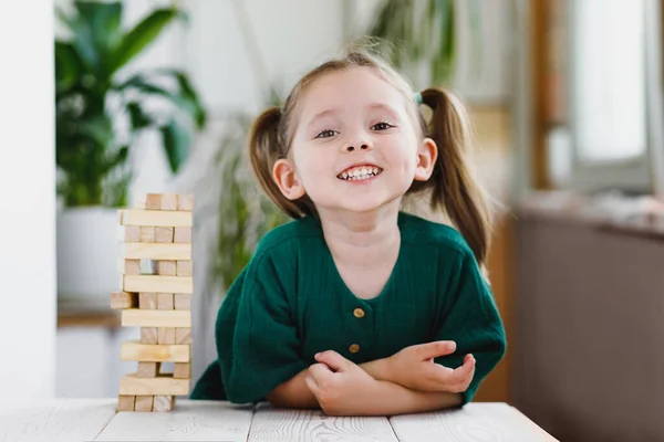 Uśmiechnięty szczęśliwy w wieku przedszkolnym dziewczyna gra Jenga i pobyt w domu, zabawny i radosny w grze, biały dzieciak radosny tej gry — Zdjęcie stockowe