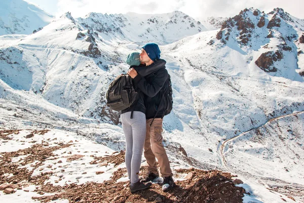 Casal jovem abraçando um ao outro em um fundo de montanhas nevadas — Fotografia de Stock