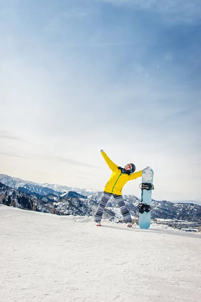 雪の山を背景に黄色のジャケットと黒のヘルメットで若い女性スノーボーダー — ストック写真