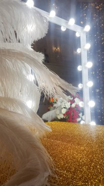 Dekoratif devekuşu tüyleri makyaj aynasının yanındaki altın bir masada.