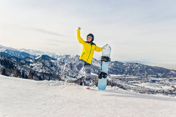 雪の山を背景に黄色のジャケットと黒のヘルメットで若い女性スノーボーダー — ストック写真