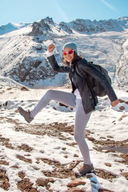 Gözlüklü genç bir kız karda dans ediyor. Kışın dağlar.