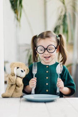 Yeşil elbiseli şirin beyaz kız elleriyle yüzünü kapatıyor. Masanın üzerinde duran tahta oyuncak kulesi..