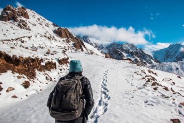 Sırt çantalı bir kadın dağlara tırmanıyor. Karda izler.