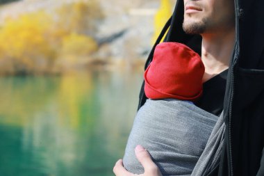 Çekici, genç bir baba ve bebeği açık havada asılıymış. İnsan çocuğunu taşıyor ve sonbahar dağ gölünde seyahat ediyor. Bebek giyme konsepti.