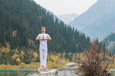 Beyazlı genç bir adam dağlarda yoga yapıyor. Poz Samasthiti namaskar