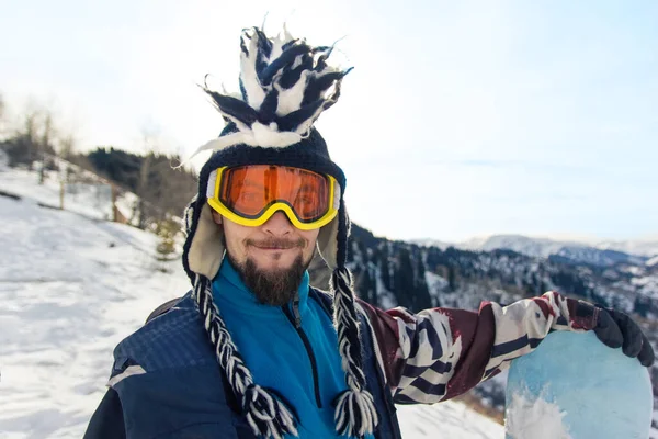 头戴莫霍克帽、留着胡子的男子滑雪板上的滑稽肖像画欣赏高山上的滑雪胜地 — 图库照片