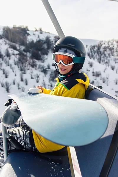 Młoda Kobieta Snowboardzistka Siedzi Wyciągu Trzymając Snowboard Patrzy Kamerę — Zdjęcie stockowe