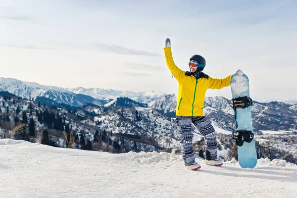 身穿黄色夹克头戴黑色头盔的年轻女子滑雪板 背景是多雪的高山 — 图库照片
