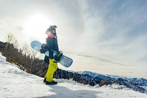 Snowboarder freerider in funny hat in the mountains is preparing to descend on the background of snowy mountains