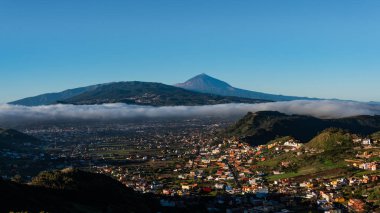 Bulutlar, mavi gökyüzü ve volkan ile büyük köy