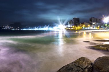 Güzel ışıklar ve kayalar üzerinde yavaş su dalgaları ile gece ünlü Ipanema Plajı