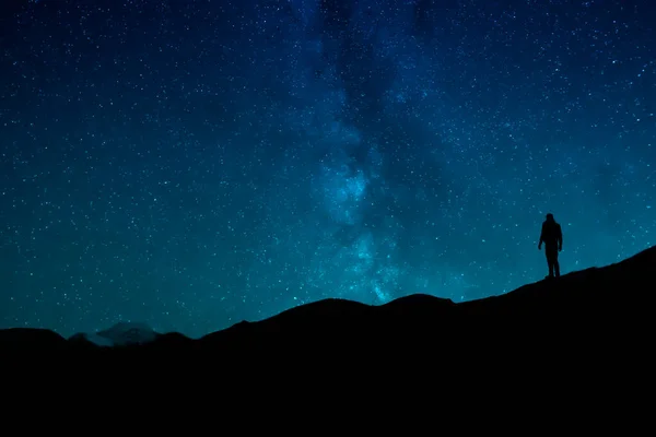 Gecenin karanlığında yıldızlı gökyüzünün altında duran insan silueti.