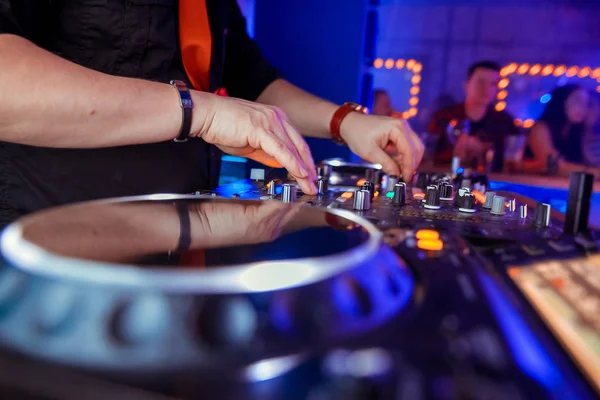 Dj mixes the track in the nightclub at party. Headphones in foreground and DJ hands in motion