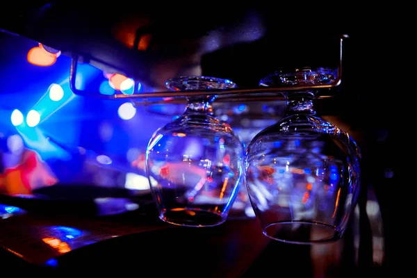 Glasses of wine. Glasses hanging above the bar in the restaurant. Empty glasses for wine. Wine and martini glasses in shelf above a bar rack in restaurant. blue lights, blue background, night life