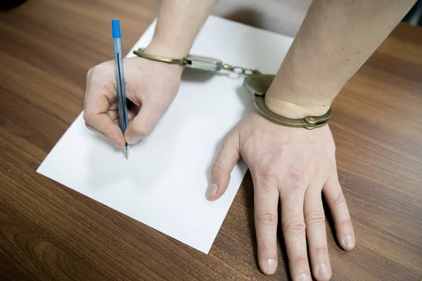 Hands of the criminal in handcuffs write a handle on paper. Sincere confession, request, statement. Justice.