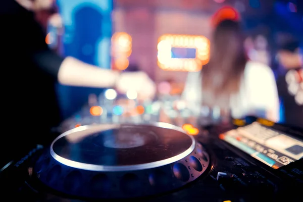 control DJ for mixing music with blurred people dancing at party in nightclub