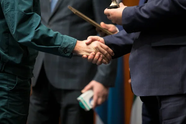 Business award. Mature businessman congratulates younger employee standing in front of the happy team