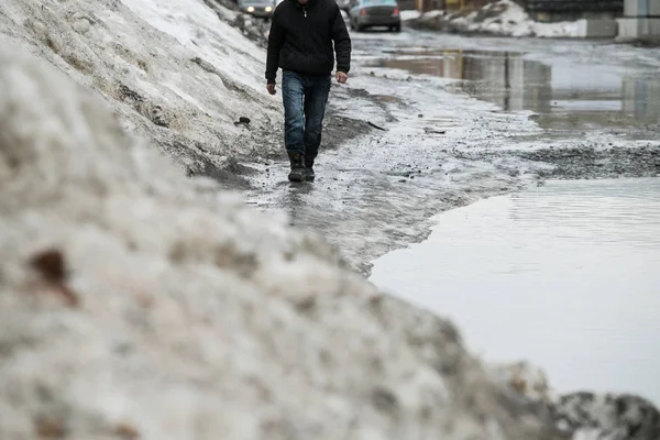 warming in early spring, snow melts turning into slush and puddles underfoot, which bypass the pedestrians walking on the sidewalk and crossing the road with wet feet