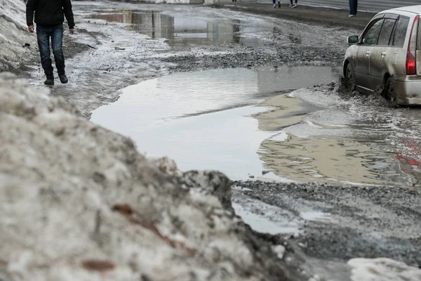 warming in early spring, snow melts turning into slush and puddles underfoot, which bypass the pedestrians walking on the sidewalk and crossing the road with wet feet