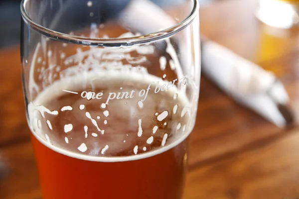 Closeup of beer in a pint glass on a table.  The glass is marked with the measurement for \