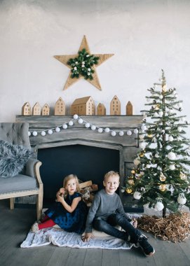 Çocuklarım - bir erkek ve bir kız şömine, yılbaşı ağacı, karton ev, rahat bir Noel dekor ve çocukların duyguları ile yürütme tarafından oturuyor musunuz