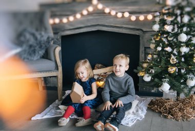 Çocuklarım - bir erkek ve bir kız şömine, yılbaşı ağacı, karton ev, rahat bir Noel dekor ve çocukların duyguları ile yürütme tarafından oturuyor musunuz