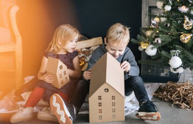Çocuklarım - bir erkek ve bir kız şömine, yılbaşı ağacı, karton ev, rahat bir Noel dekor ve çocukların duyguları ile yürütme tarafından oturuyor musunuz