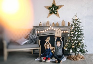 Çocuklarım - bir erkek ve bir kız şömine, yılbaşı ağacı, karton ev, rahat bir Noel dekor ve çocukların duyguları ile yürütme tarafından oturuyor musunuz