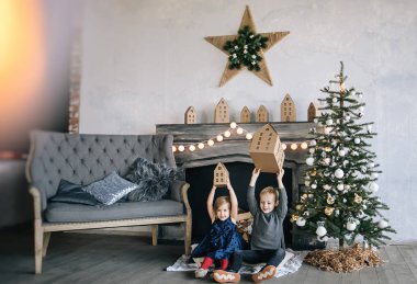 Çocuklarım - bir erkek ve bir kız şömine, yılbaşı ağacı, karton ev, rahat bir Noel dekor ve çocukların duyguları ile yürütme tarafından oturuyor musunuz
