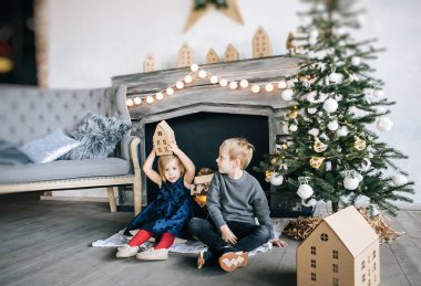 Çocuklarım - bir erkek ve bir kız şömine, yılbaşı ağacı, karton ev, rahat bir Noel dekor ve çocukların duyguları ile yürütme tarafından oturuyor musunuz