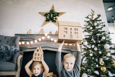 Çocuklarım - bir erkek ve bir kız şömine, yılbaşı ağacı, karton ev, rahat bir Noel dekor ve çocukların duyguları ile yürütme tarafından oturuyor musunuz