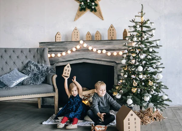 Çocuklarım - bir erkek ve bir kız şömine, yılbaşı ağacı, karton ev, rahat bir Noel dekor ve çocukların duyguları ile yürütme tarafından oturuyor musunuz