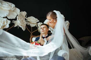 Gelin ve damat güzel elbise beyaz vintage iskemlede ve sarılma - Studio bir arka planda büyük beyaz çiçek düğün fotoğraf