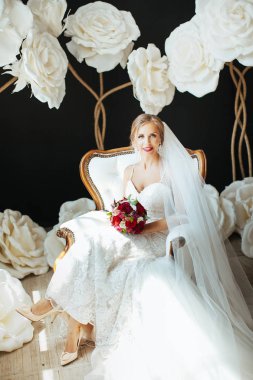 çok güzel bir elbise içinde bir gelin gelin buketi onun elinde - düğün fotoğraf Studio büyük beyaz çiçekler bir arka plan üzerinde tutan bir beyaz vintage sandalyede oturuyor
