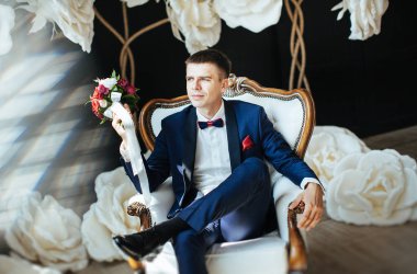 damat şık mavi elbiseli bir beyaz vintage sandalye - Studio bir arka planda beyaz büyük çiçek düğün fotoğraf oturuyor