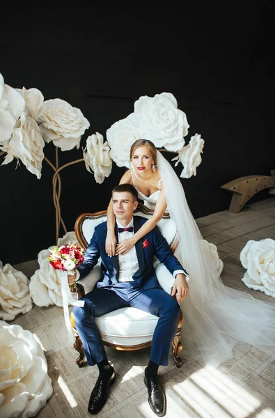 Bruden Omfamnar Försiktigt Brudgummen Bröllopsfoto Studion Bakgrund Vita Stora Blommor — Stockfoto