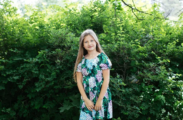金发碧眼的少女在一个花礼服摆姿势在一个绿色的公园 积极的女学生微笑 — 图库照片