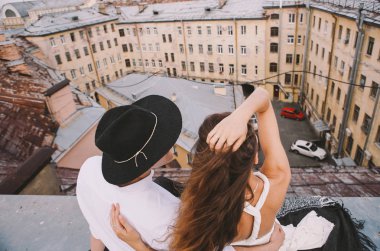 Çatıda sarılma ve gülüyor, şehrin pozitif ve samimi duygular aşk çatısı görünümünden bir yolda seven çift - beyaz elbiseli bir kız - ve şapkalı bir adam