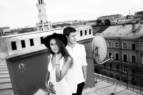 loving couple - a girl in a white dress and a hat and a guy - on a walk on the roof hugging and laughing, the view from the roof of the city, positive and sincere emotions of love