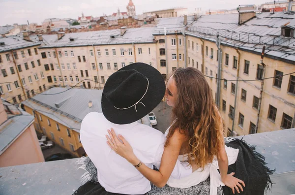 loving couple - a girl in a white dress and  a guy in hat - on a walk on the roof hugging and laughing, the view from the roof of the city, positive and sincere emotions of love