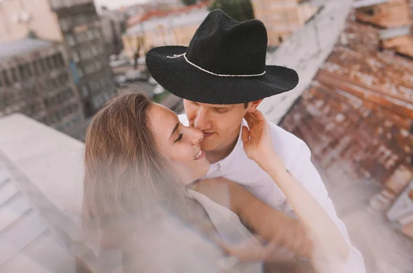 loving couple - a girl in a white dress and  a guy in hat - on a walk on the roof hugging and laughing, the view from the roof of the city, positive and sincere emotions of love